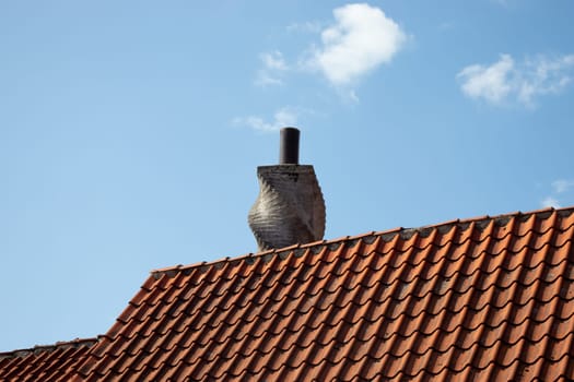Chimney on the roof of an old houses. Tiled roof and blue sky. Heating systen.