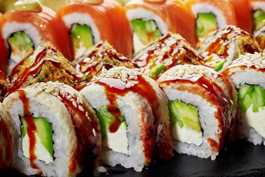 Detailed closeup view of appetizing uramaki rolls with eel drizzled with savory unagi sauce and sesame seeds, served on black slate board. Vibrant Japanese sushi platter