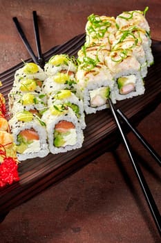 Exquisite sushi rolls filled with shrimp and salmon garnished with greens and drops of spicy mayo presented on stylish wooden tray with black chopsticks, ready for delightful meal. Japanese cuisine