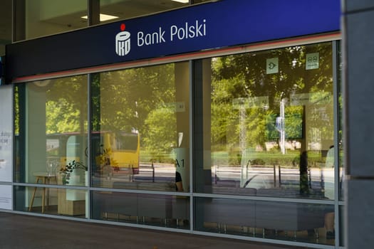 Wroclaw, Poland - August 4, 2023: A PKO Bank Polski branch with ATMs and glass windows is pictured on a clear, sunny morning in an urban setting. The reflection of trees in the glass adds a pleasant touch to the scene.