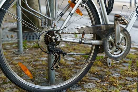 A bicycle is parked on a city sidewalk, leaning on a metal rack. The scene conveys urban transportation and the use of bicycles for commuting.