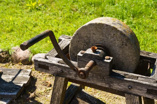 A well-worn grinding wheel sits idle on a rustic wooden stand, with a metal hammer resting atop, basking in the sunshine of a serene day.