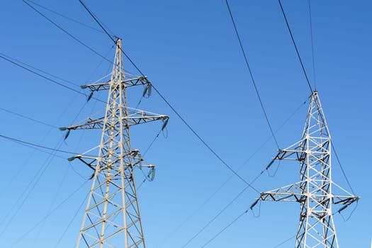 High voltage pylons stand tall against a clear blue sky, carrying electrical wires across the landscape.
