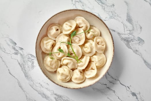 Appetizing plump freshly boiled dumplings with savory stuffing garnished with microgreens served in ceramic bowl, placed on marble surface