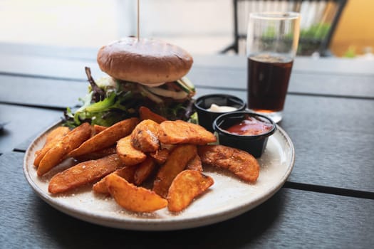 Plate with burger and french fries, ketchup and mayonnaise and cola on the table in the restaurant.
