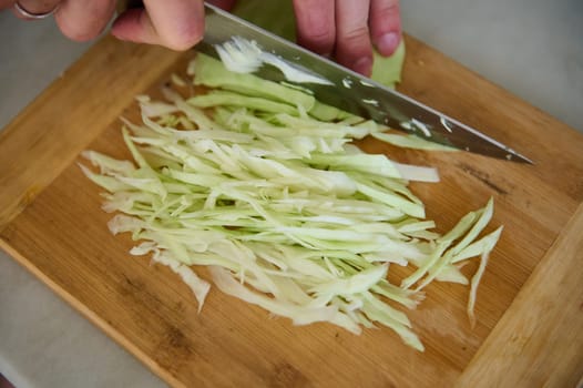 Close-up view from above of a man chopping raw fresh cabbage on a wooden board