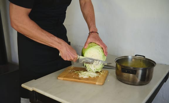 Close-up male chef chopping raw fresh cabbage on a wooden board in rustic home kitchen. Food concept