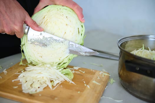 Close-up chef man using kitchen knife, slicing cutting raw fresh cabbage on a wooden board, preparing raw organic vegan salad