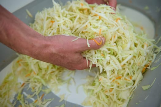 Close-up view from above of hands of a chef man mixing raw fresh sliced cabbage, seasoning and preparing healthy vegan salad