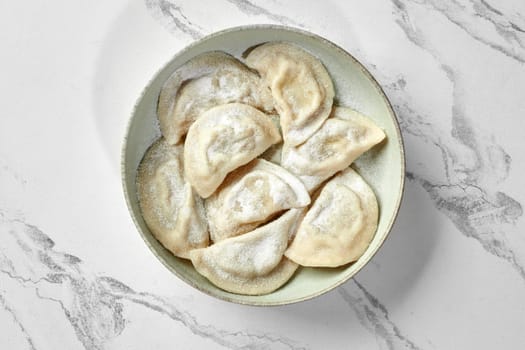 Delicious varenyky with sweet curd filling sprinkled with powdered sugar, served on ceramic rustic bowl against marble background. Traditional Ukrainian cuisine