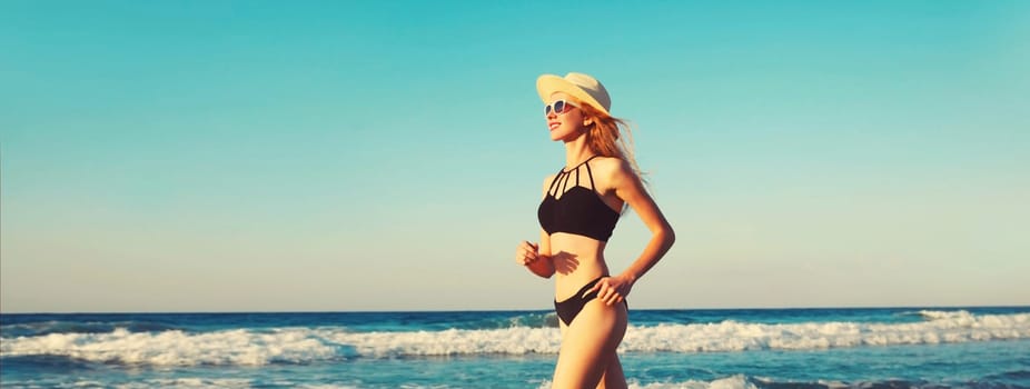 Summer vacation, happy smiling woman walking running in bikini swimsuit and straw hat on the beach on sea coast with waves background on sunny day, blue sky