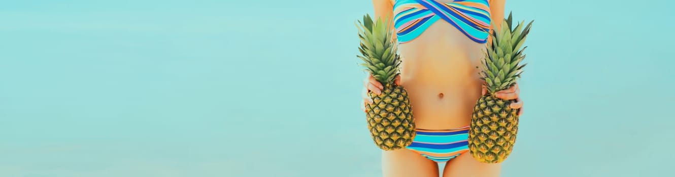 Summer vacation, close up beautiful young woman in bikini swimsuit with two pineapples on the beach on sea coast background, advertising banner copy space
