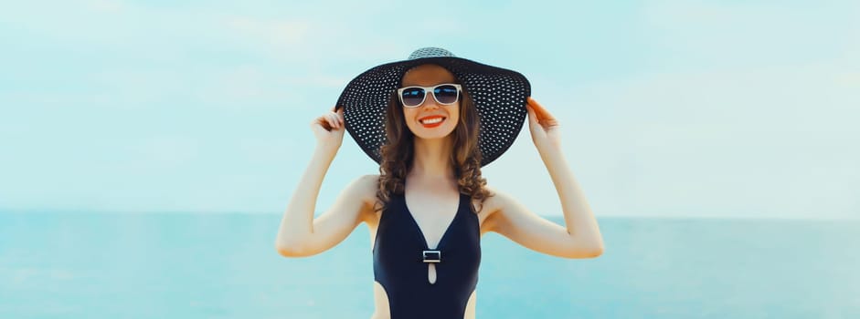 Summer vacation, beautiful happy smiling woman in black bikini swimsuit and straw hat on the beach on sea coast background