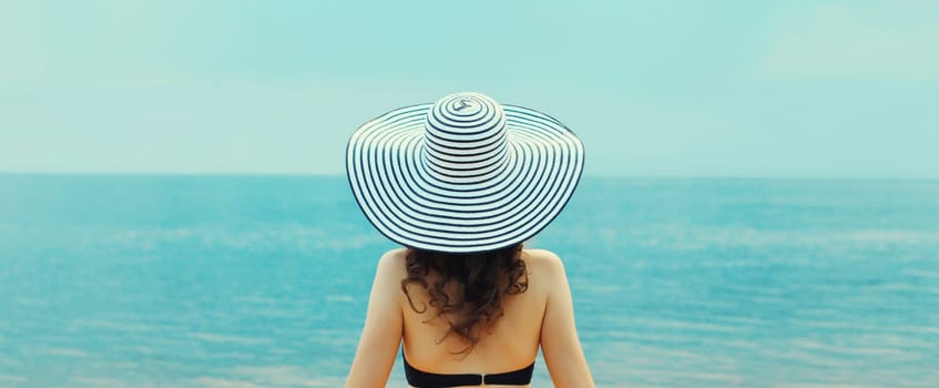 Summer vacation, rear view of beautiful relaxed young woman in straw hat on the beach on sea background, looking at water