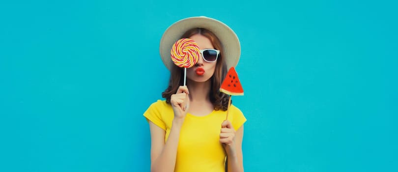 Summer portrait of stylish young woman with sweet juicy lollipop or ice cream shaped slice of watermelon wearing straw hat on blue studio background