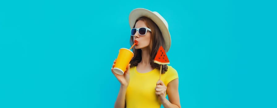 Summer portrait of young woman drinking juice with sweet juicy lollipop or ice cream shaped slice of watermelon wearing straw hat on blue background