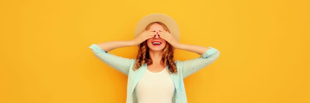 Stylish surprised young woman covering her eyes with hands wearing summer straw hat, jean jacket posing on yellow background