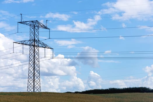 Electricity concept. High voltage power line pylons, electrical tower on a green field with blue sky. High quality photo