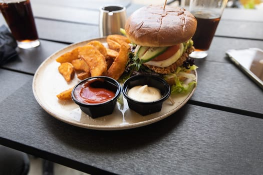 Plate with burger and french fries, ketchup and mayonnaise and cola on the table in the restaurant.