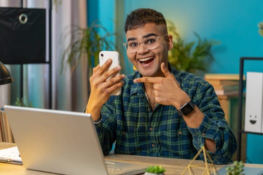 Smiling happy man using smartphone application online pointing showing like thumbs up remote distance job working from home office. Guy freelancer recommends to use a good mobile program. Lifestyle