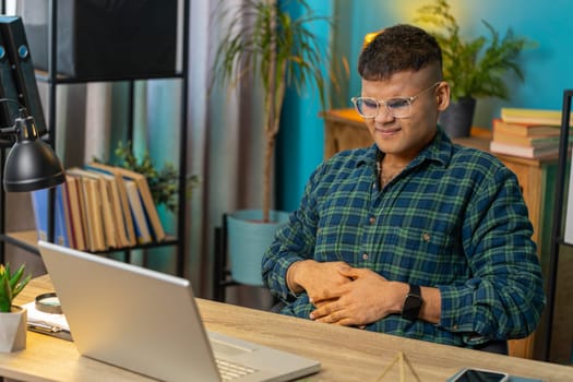 Indian man feeling sudden strong abdominal stomach ache gastritis problem. Guy having symptom poisoning diarrhea indigestion peptic ulcer pancreatitis sitting at home office table workplace. Lifestyle