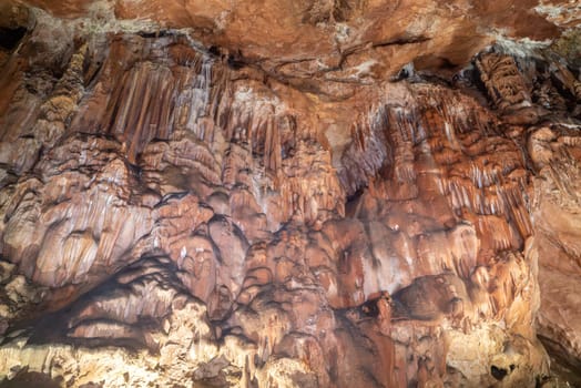 A cave with a lot of brown and white rock formations. The rock formations are very large and the cave is very dark