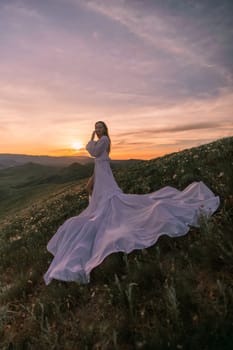 A woman in a long white dress is standing on a hillside, with the sun setting in the background. The scene is serene and peaceful, with the woman's dress flowing in the wind