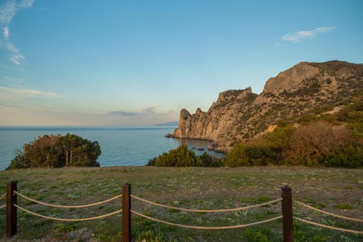 A beautiful view of the ocean with a rocky cliff in the background. The sky is clear and the sun is setting