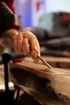 Manufacturer meticulously carving intricate designs into wood using chisel and hammer in carpentry shop. Carpenter in woodworking workshop shaping wooden pieces with tools, close up shot