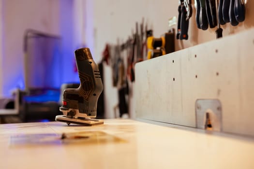 Close up shot of electric router on workbench in assembly shop with woodworking tools on rack in background. Focus on hand powered gear used for cutting wood in carpentry studio