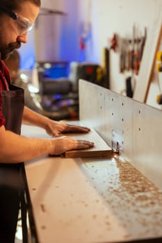 Carpenter puts wood block through spindle moulder wearing safety glasses to avoid injury. Cabinetmaker using heavy machinery to craft furniture using protective gear to prevent accidents