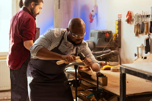 African american man wearing protection equipment while carving wood to prevent workplace accidents. Cabinetmaker equipped with safety glasses while using chisel and hammer, sculpting wooden surface