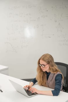 Caucasian woman scientist typing on laptop. White board with formulas. Vertical photo