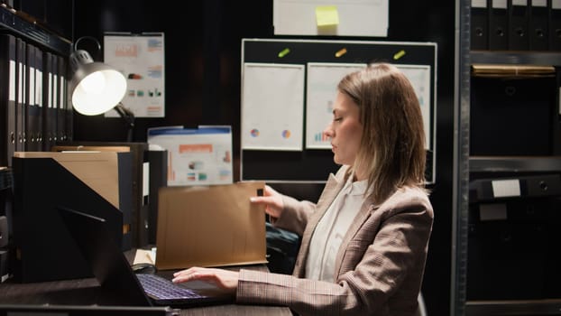 Close-up of caucasian female detective closing laptop and folder, leaving her workstation. After obtaining information to solve criminal investigation, policewoman stands and exits the evidence room.