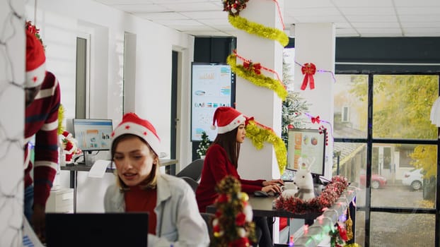 African american employee working during Christmas season in festive decorated office, showing manager task progress. Workers in multiethnic diverse xmas ornate workplace