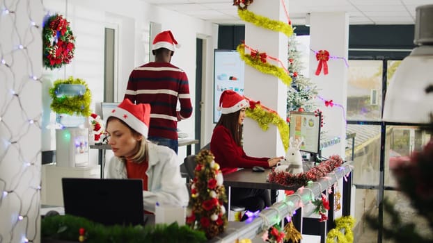 African american staff member working during Christmas season in festive decorated office, showing supervisor task progress. Multiethnic diverse team in xmas ornate workplace during holiday season