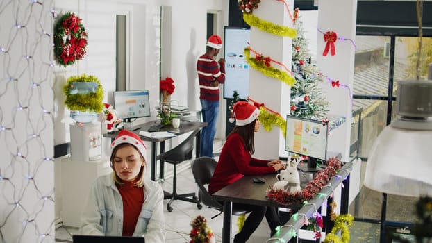 Asian staff member working during Christmas season in festive decorated office, showing supervisor audit progress. Accountant solving task in diverse xmas ornate workplace during holiday season