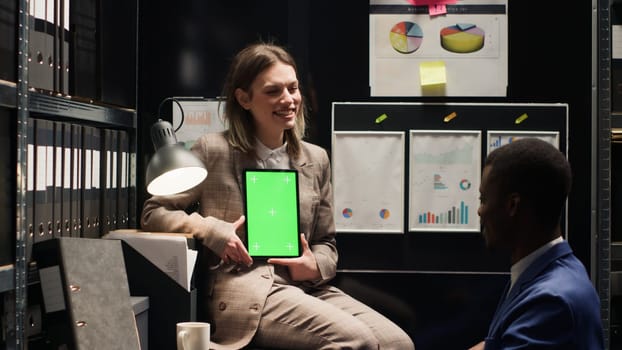 Female inspector speaking with policeman while vertically holding digital tablet with isolated chromakey mockup template. Multiethnic investigators utilizing smart device with greenscreen display.