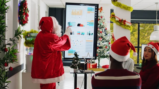 Public speaker dressed as Santa Claus doing presentation in front of company employees in Christmas holiday season. Coworkers in xmas adorn meeting room learning how to advance their career