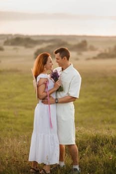 A couple in love in white clothes in a field at a red sunset.