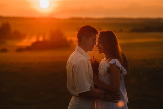 A couple in love in white clothes in a field at a red sunset.