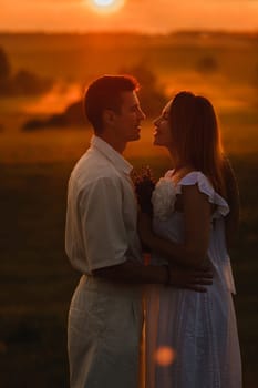 A couple in love in white clothes in a field at a red sunset.