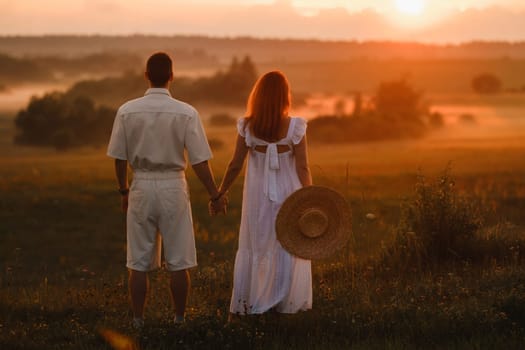 A couple in love in white clothes in a field at a red sunset.