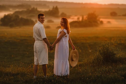 A couple in love in white clothes in a field at a red sunset.