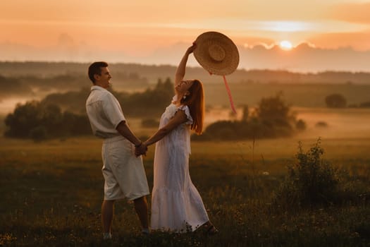 A couple in love in white clothes in a field at a red sunset.