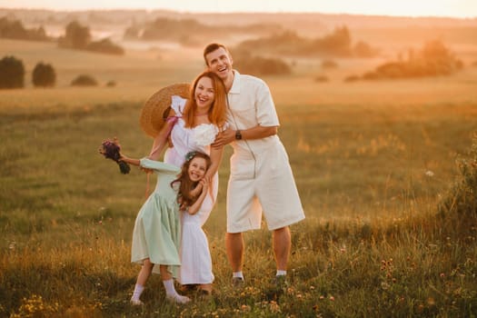 A beautiful happy family of three is standing in a field at sunset.