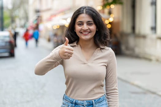 Like. Happy Indian woman raises thumbs up agrees with something gives positive reply recommends advertisement likes good idea feedback celebrating success victory outdoors. Girl walking on city street