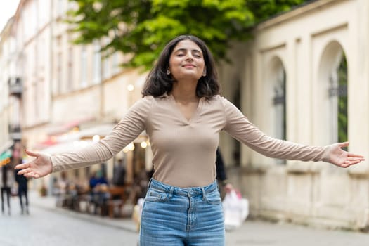 Indian young woman taking a deep breath of fresh air, relaxing, taking a break, resting, meditating, calm down outdoors. Hispanic girl enjoying happy day walking on urban city street. Town lifestyles