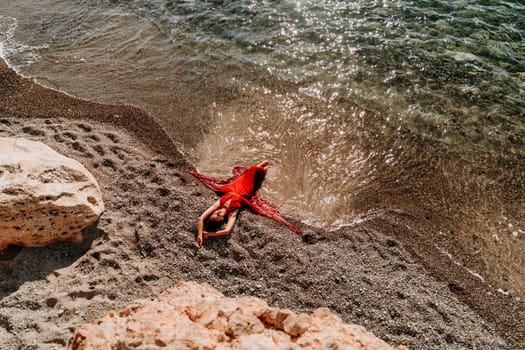 Woman red dress sea. Female dancer in a long red dress posing on a beach with rocks on sunny day.