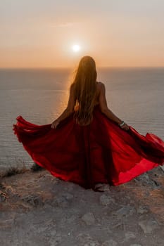 Woman sunset sea red dress, back view a happy beautiful sensual woman in a red long dress posing on a rock high above the sea on sunset